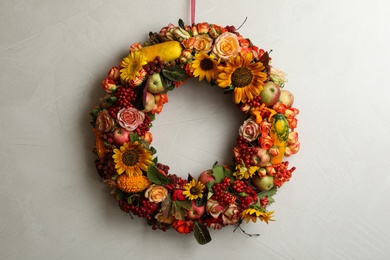 Photo of Beautiful autumnal wreath with flowers, berries and fruits hanging on light grey background. Space for text