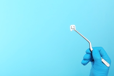 Photo of Dentist holding small plastic tooth with tweezers on color background. Space for text