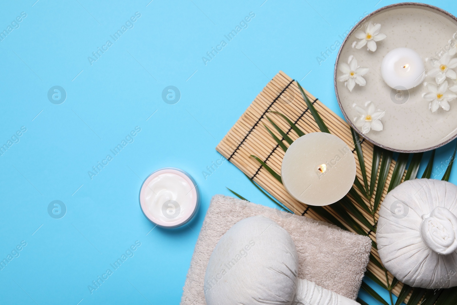 Photo of Flat lay composition with spa products, burning candle and beautiful flowers on light blue background. Space for text