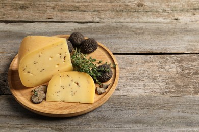 Photo of Delicious cheese, fresh black truffles and thyme on wooden table. Space for text