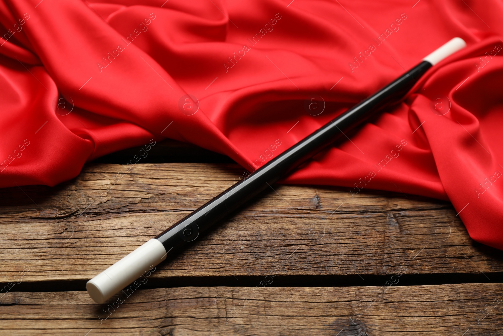 Photo of Beautiful black magic wand and red fabric on wooden table