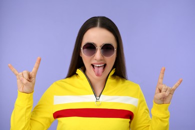 Photo of Happy woman in sunglasses showing her tongue and rock gesture on violet background