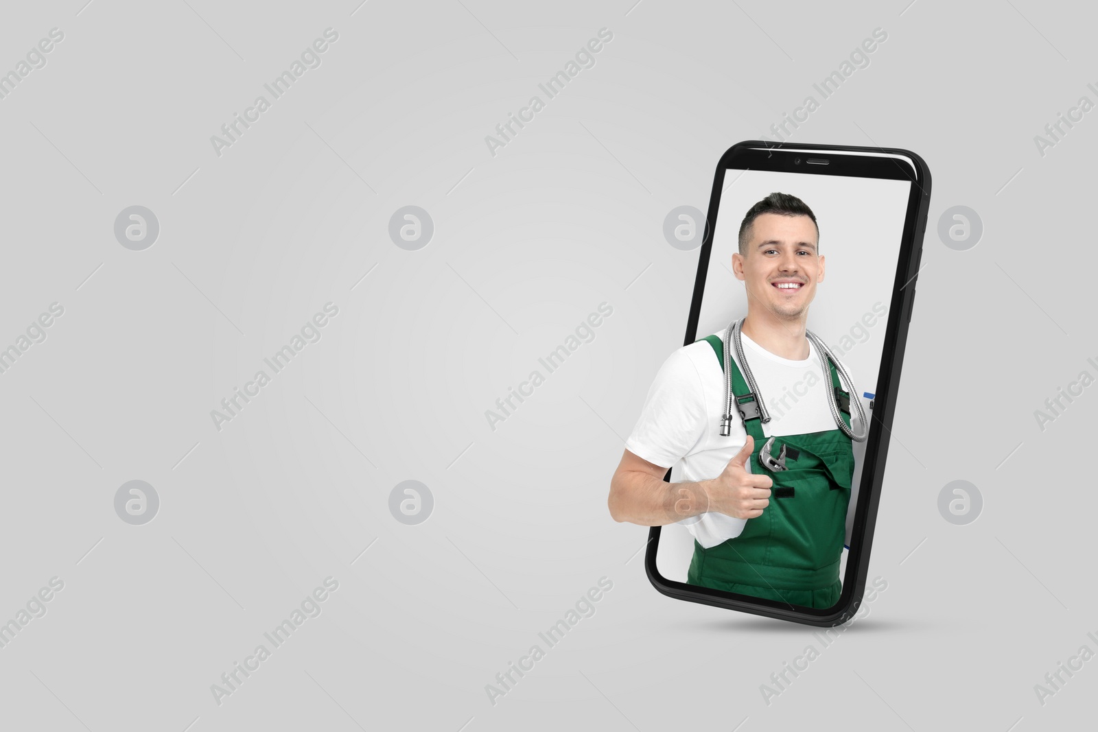 Image of Plumber looking out of smartphone and showing thumbs up on light grey background. Space for text