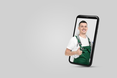 Image of Plumber looking out of smartphone and showing thumbs up on light grey background. Space for text