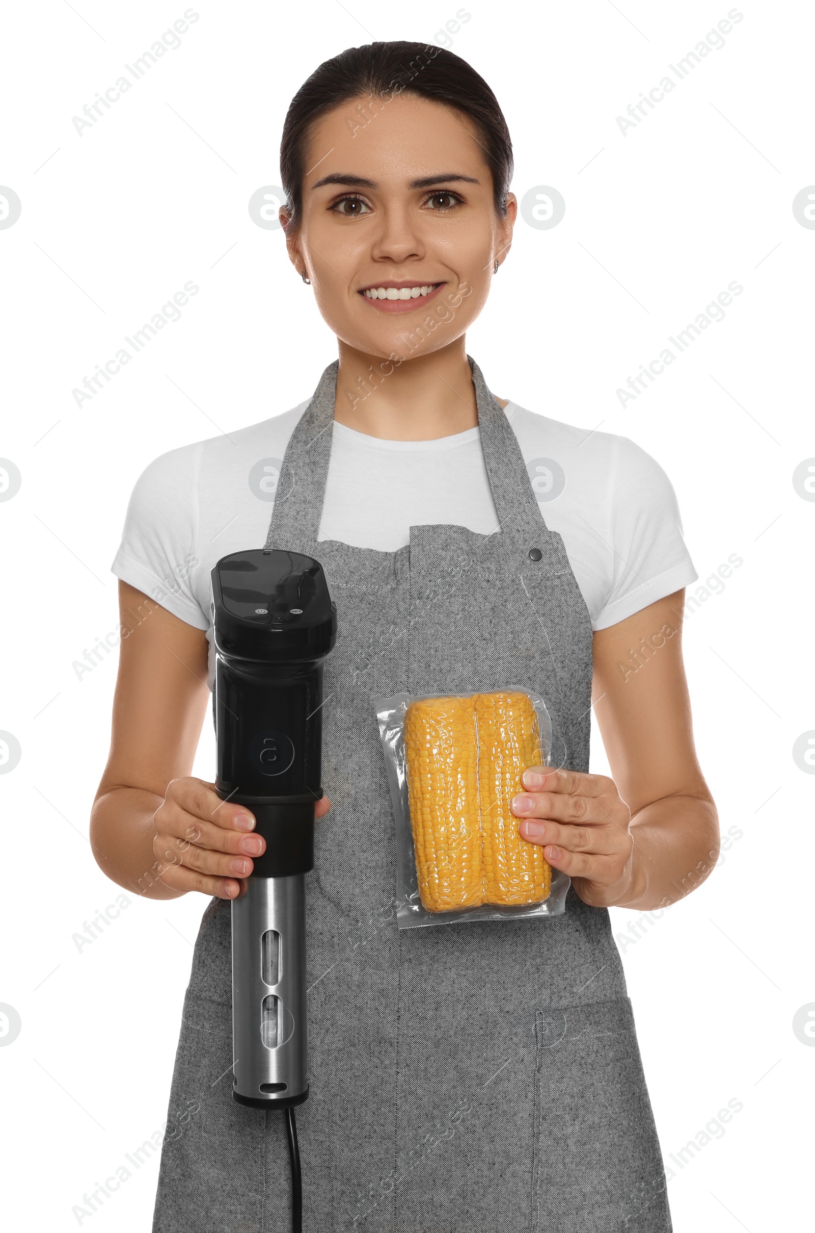 Photo of Beautiful young woman holding sous vide cooker and corn in vacuum pack on white background