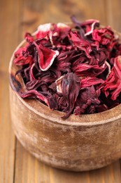 Photo of Dry hibiscus tea in bowl on wooden table, closeup