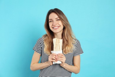 Young woman with delicious shawarma on turquoise background