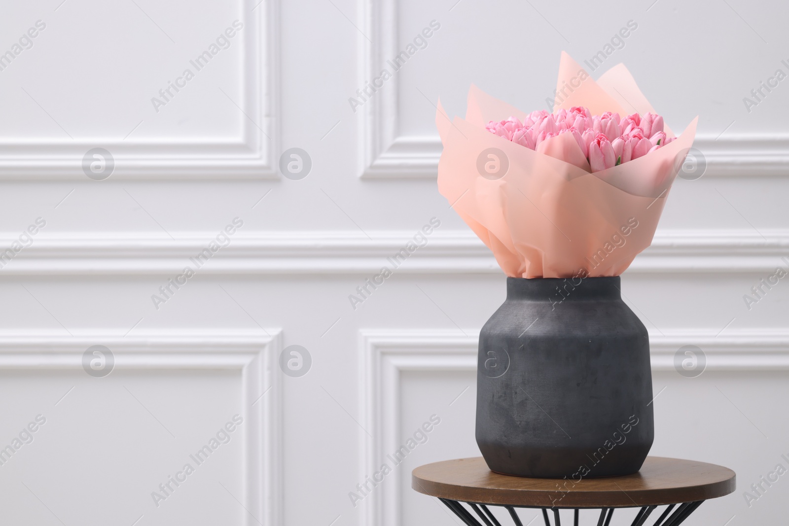 Photo of Bouquet of beautiful pink tulips in vase on wooden table near white wall, space for text