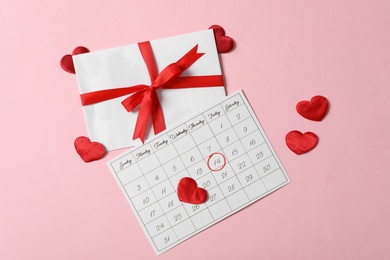 Calendar with marked Valentine's Day, gift and red hearts on pink background, flat lay