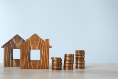 Photo of House models and stacked coins on wooden table against light blue background