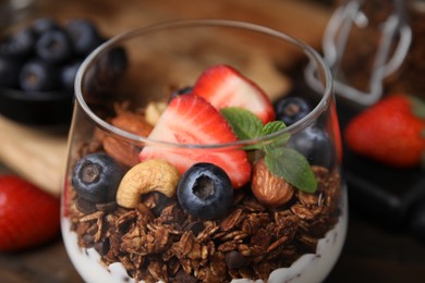 Photo of Tasty granola with berries, nuts and yogurt in glass on table, closeup