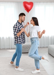 Photo of Young couple dancing with air balloon at home. Celebration of Saint Valentine's Day