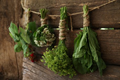 Photo of Bunches of different beautiful dried flowers hanging on rope near wooden wall