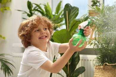 Photo of Cute little boy spraying beautiful green plant at home. House decor