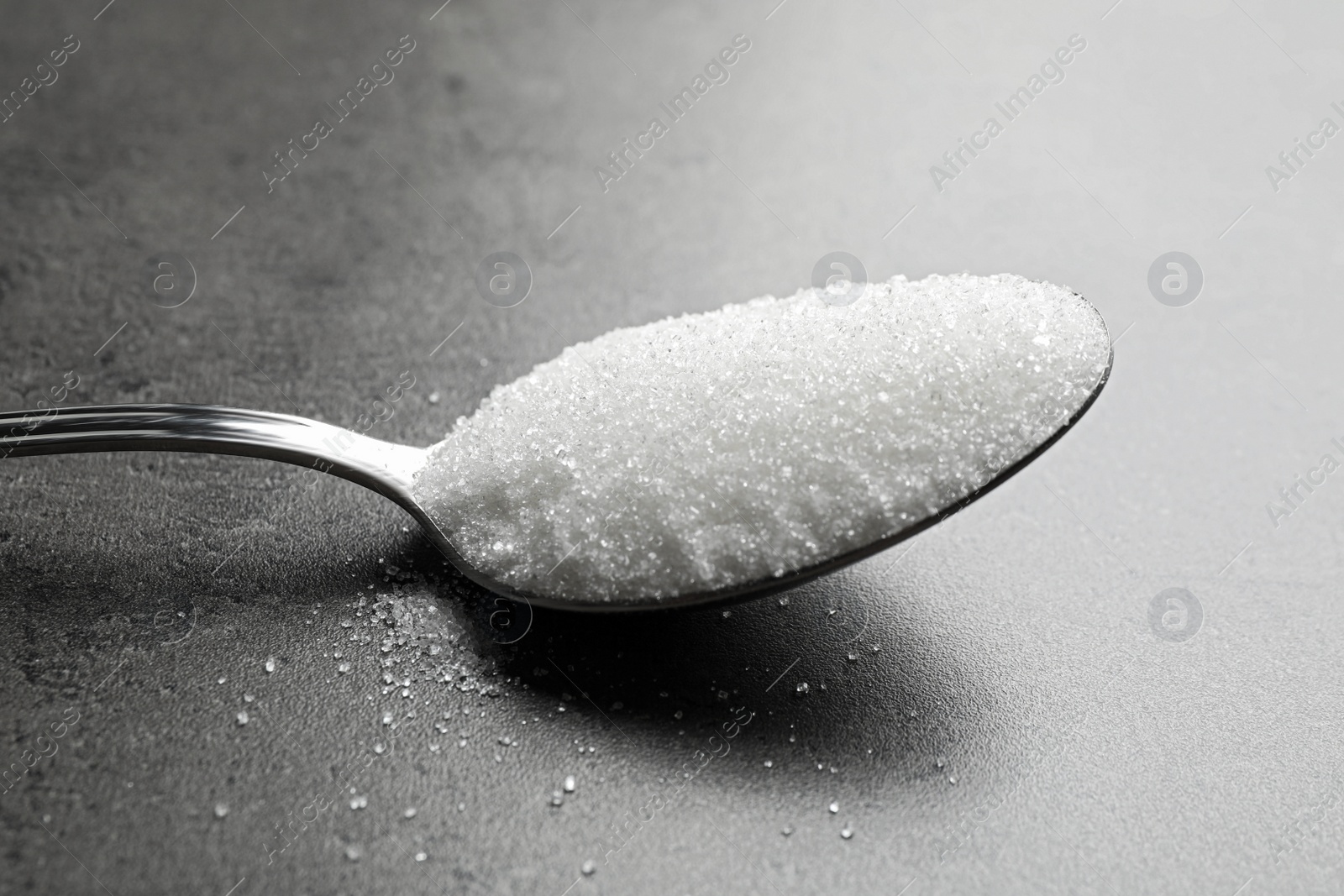 Photo of Spoon of white sugar on grey table, closeup