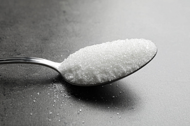 Photo of Spoon of white sugar on grey table, closeup