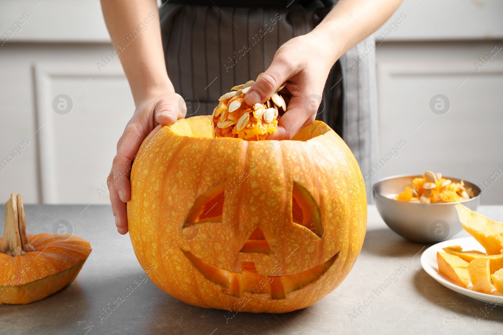 Photo of Woman making pumpkin head Jack lantern for Halloween at light table indoors, closeup