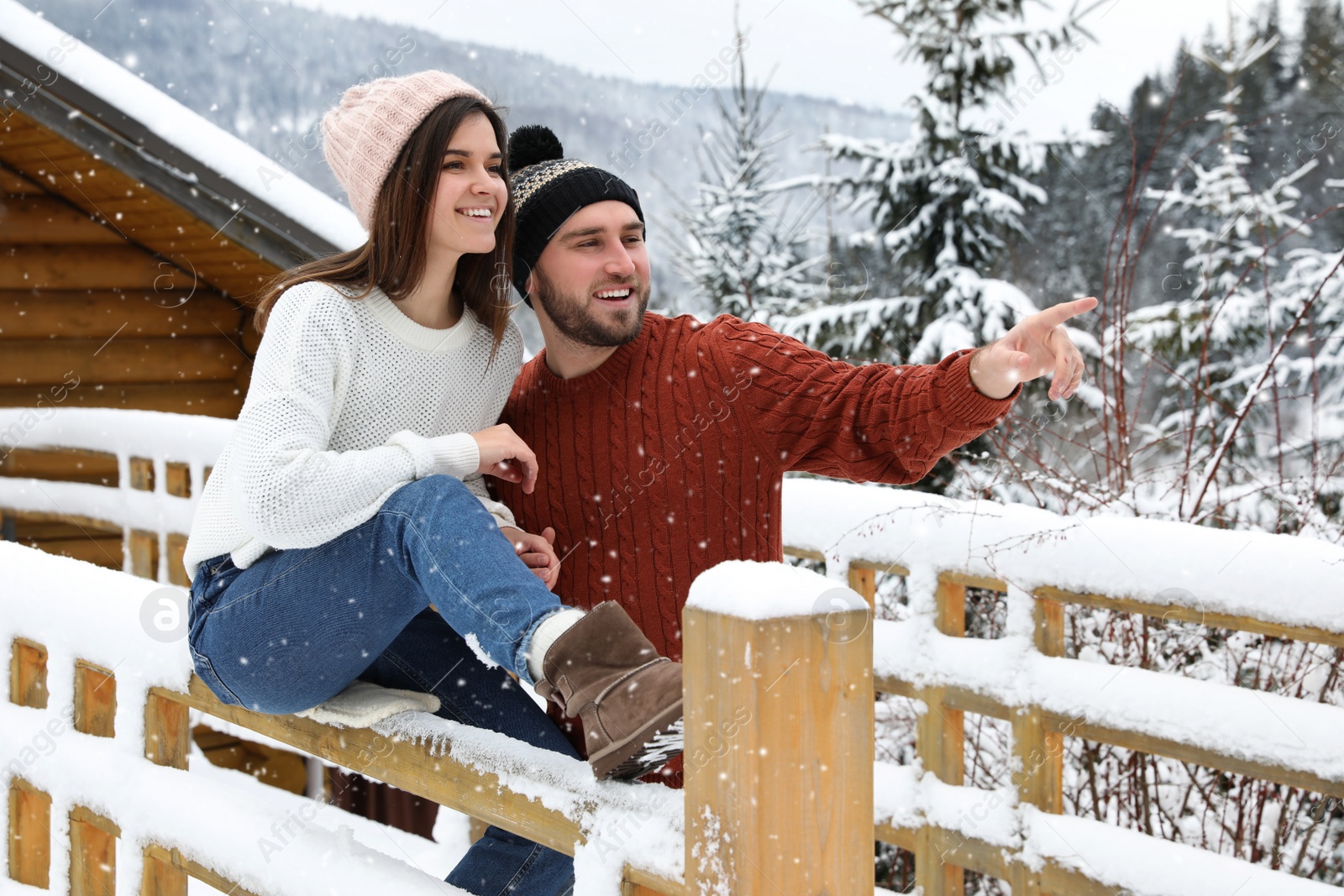 Photo of Happy couple near snowy wooden railing outdoors. Winter vacation