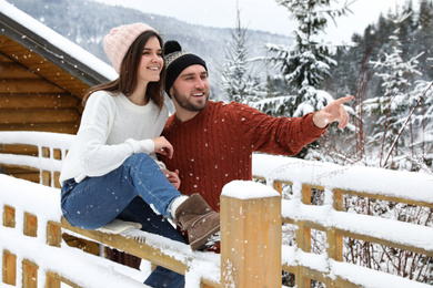 Happy couple near snowy wooden railing outdoors. Winter vacation