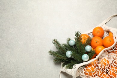 Christmas composition with fresh tangerines in mesh bag on light background, flat lay. Space for text