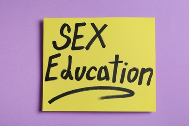 Photo of Note with phrase "SEX EDUCATION" on violet background, top view