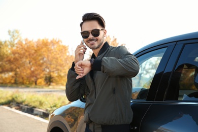 Photo of Young man checking time while talking on phone near modern car, outdoors