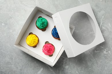 Box with different cupcakes on grey table, top view