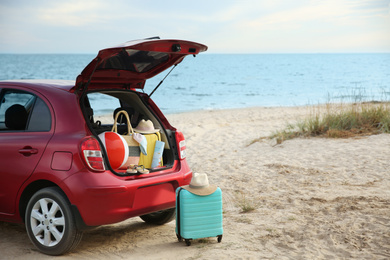 Photo of Red car luggage on beach, space for text. Summer vacation trip