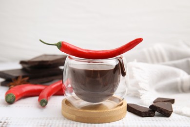 Glass of hot chocolate with chili pepper on white wooden table