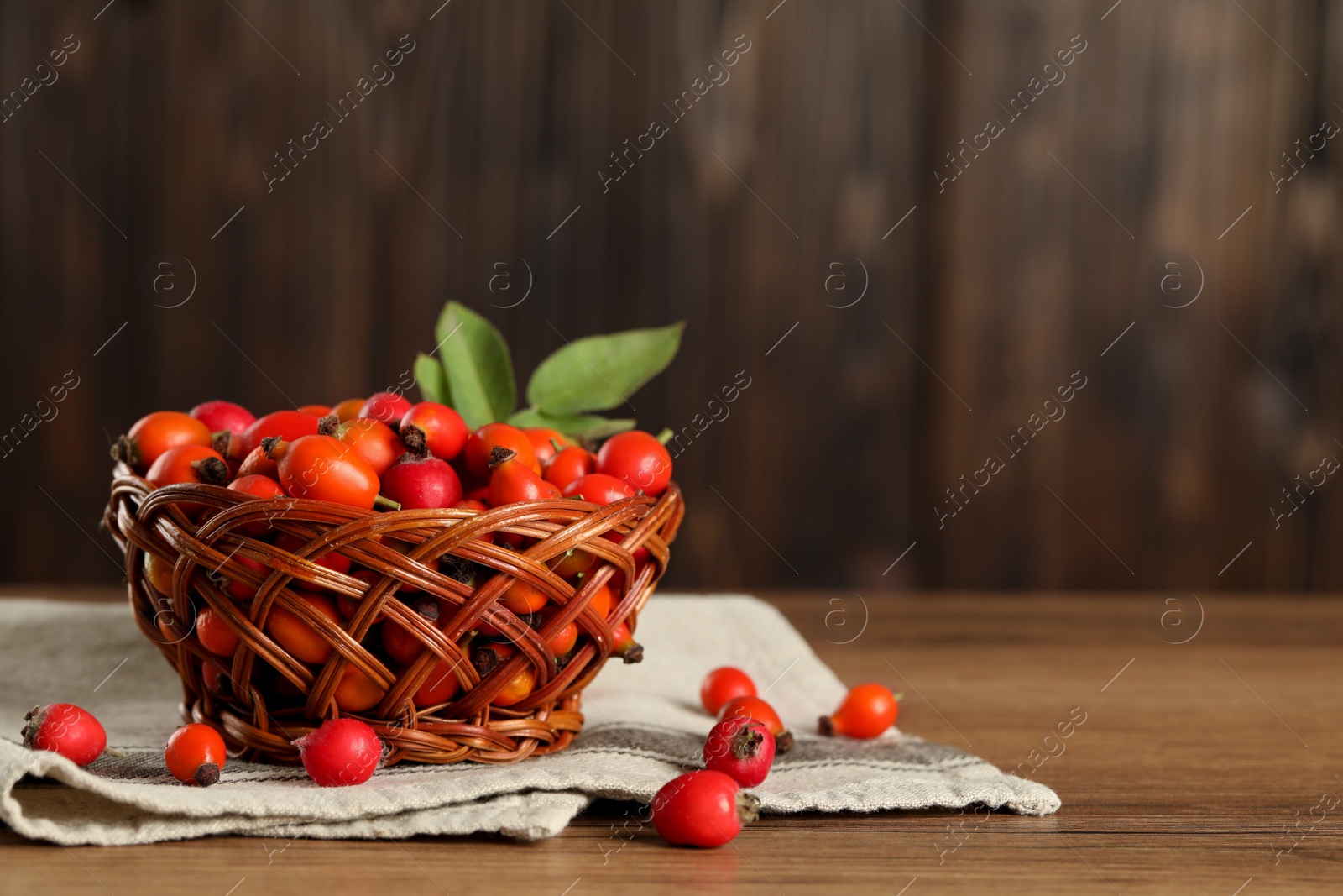 Photo of Ripe rose hip berries with green leaves on wooden table. Space for text