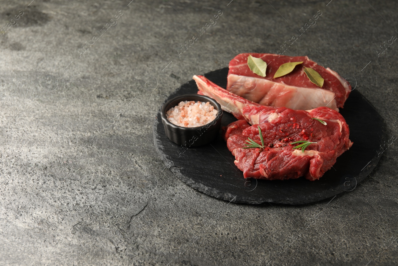 Photo of Pieces of raw beef meat and spices on grey textured table. Space for text