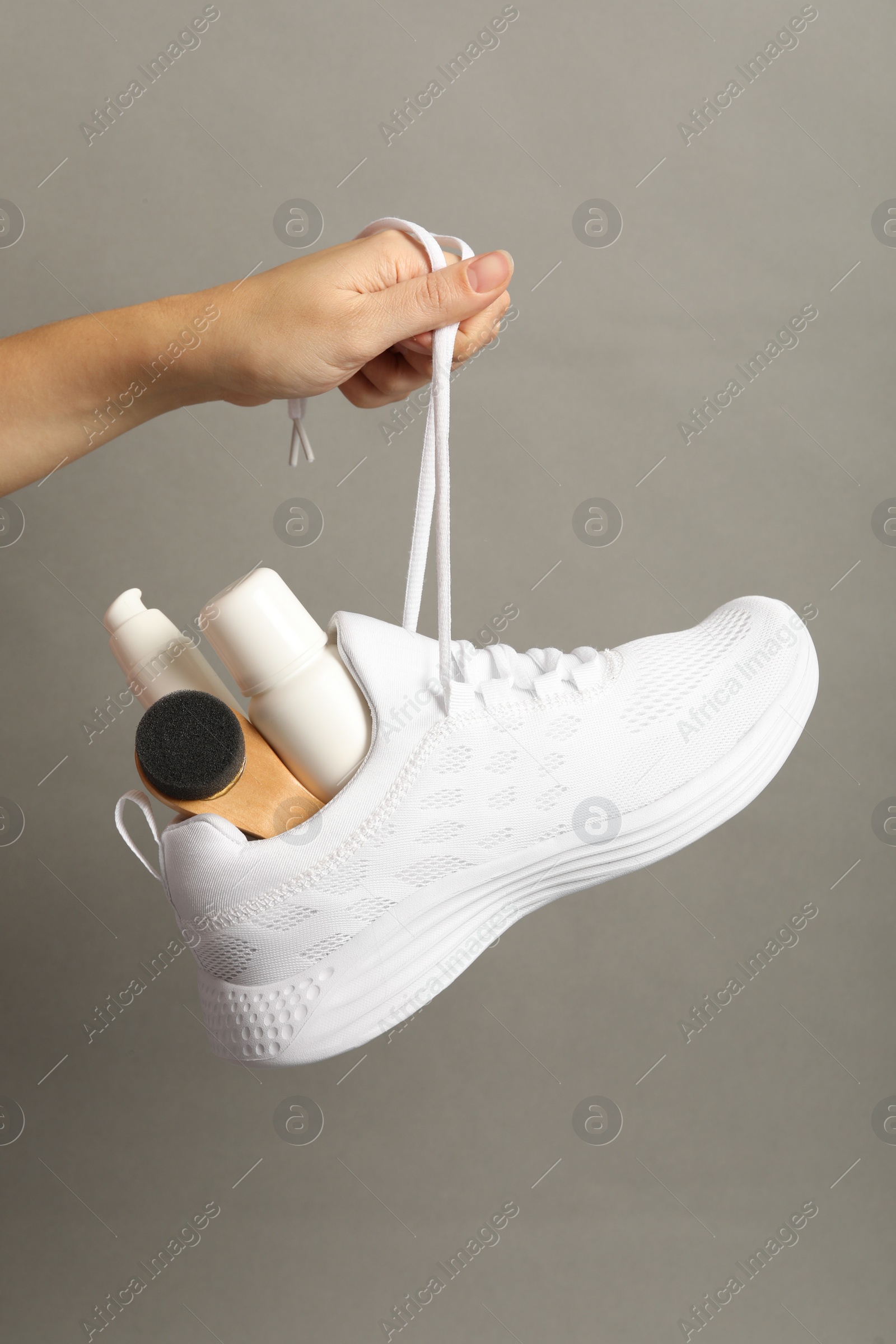 Photo of Woman holding stylish footwear with shoe care accessories on grey background, closeup