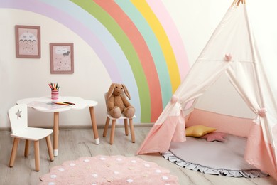 Photo of Cute child's room interior with stylish furniture, toy tent and rainbow art on wall
