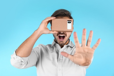 Photo of Young man using cardboard virtual reality headset on color background