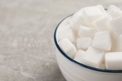 Photo of Bowl with sugar cubes on grey table, closeup. Space for text