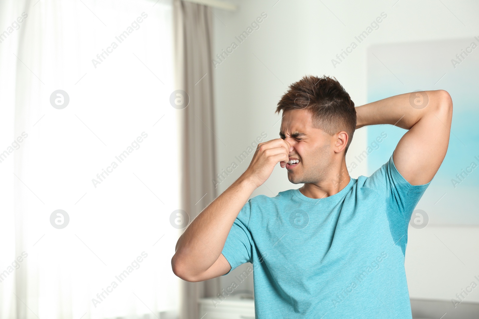 Photo of Young man with sweat stain on his clothes indoors, space for text. Using deodorant