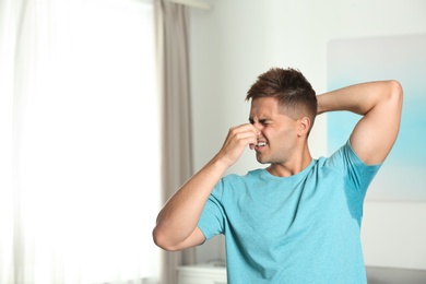 Photo of Young man with sweat stain on his clothes indoors, space for text. Using deodorant