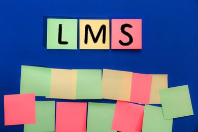 Image of Learning management system. Colorful sticky notes with abbreviation LMS on blue background, top view