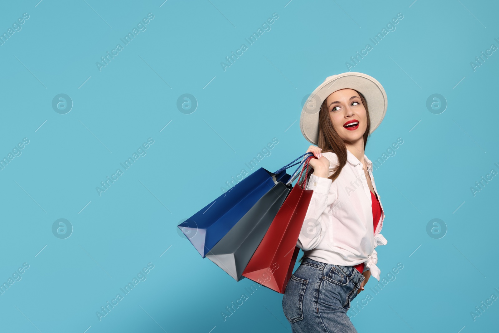 Photo of Stylish young woman with shopping bags on light blue background, space for text