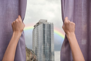 Image of Woman opening curtains and seeing beautiful rainbow in sky through window, closeup