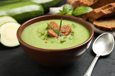 Photo of Tasty homemade zucchini cream soup served on black table