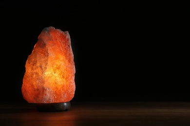 Photo of Himalayan salt lamp on table against black background. Space for text