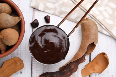 Photo of Measuring cup with tasty tamarind sauce and fresh pods on white wooden table, flat lay