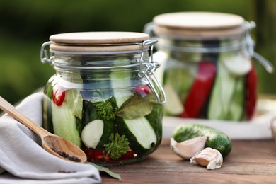 Jars of delicious pickled cucumbers and ingredients on wooden table, closeup. Space for text