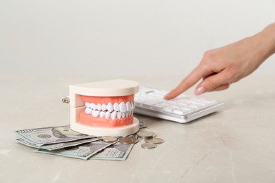 Photo of Woman using calculator near educational dental typodont model and money at light grey table, closeup. Expensive treatment