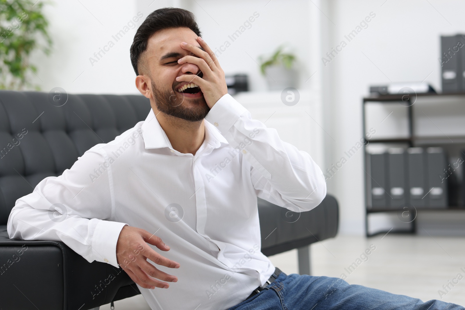 Photo of Handsome young man laughing near sofa in office