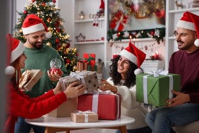 Photo of Christmas celebration. Happy friends in Santa hats exchanging gifts at home