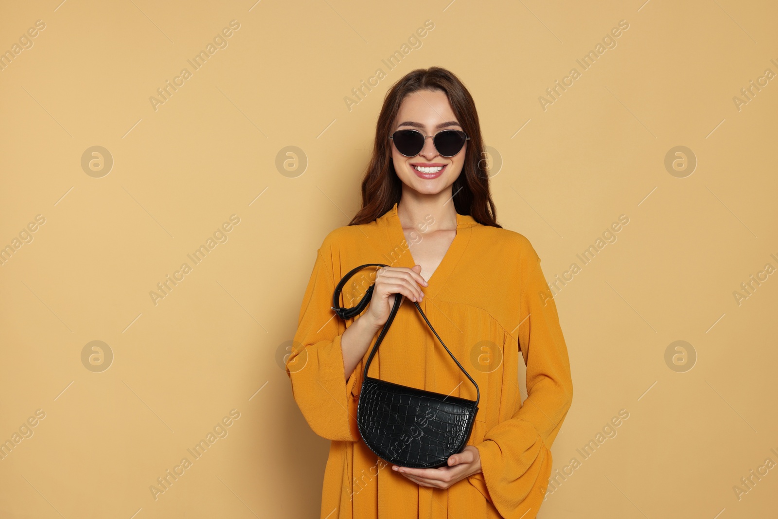 Photo of Beautiful young woman in fashionable outfit with stylish bag on beige background, space for text