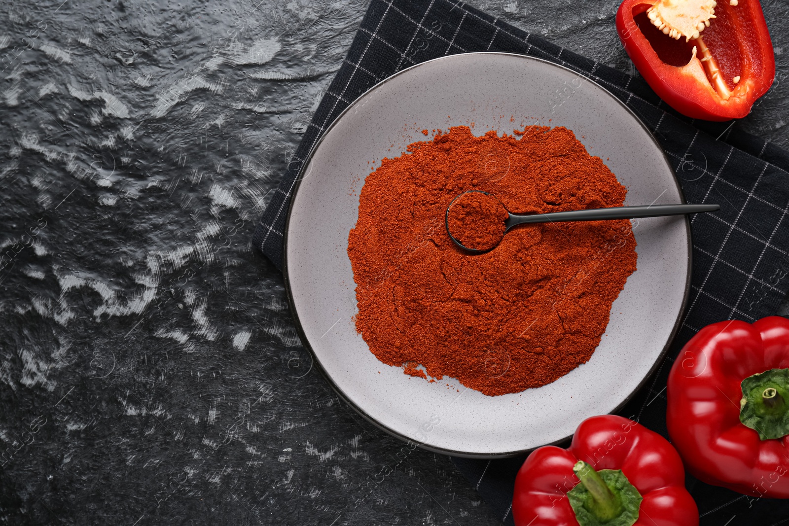 Photo of Plate of aromatic paprika and fresh peppers on black textured table, flat lay. Space for text