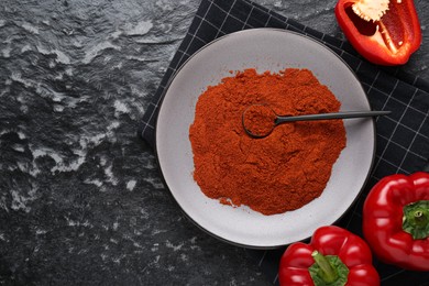 Plate of aromatic paprika and fresh peppers on black textured table, flat lay. Space for text